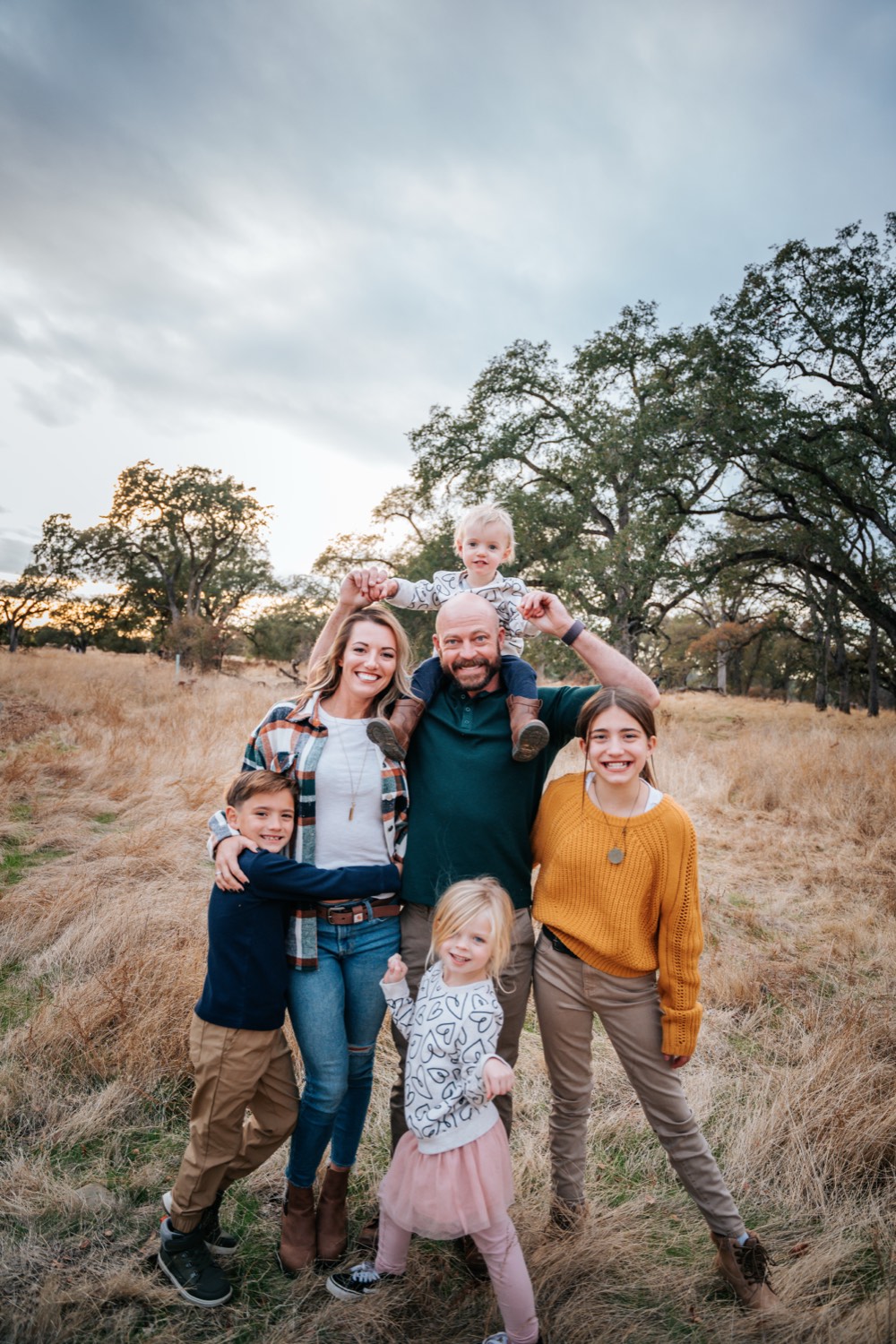 Ashley and her family smiling together in a field of golden grass under oak trees